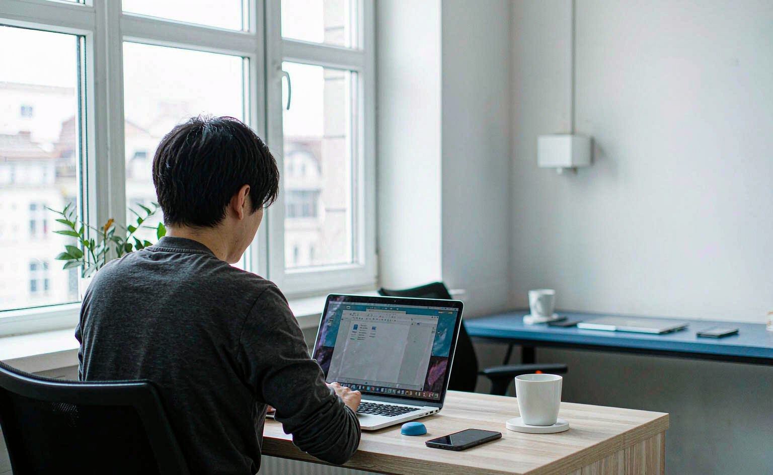 Team member working at a laptop in a bright modern office workspace, seen from behind