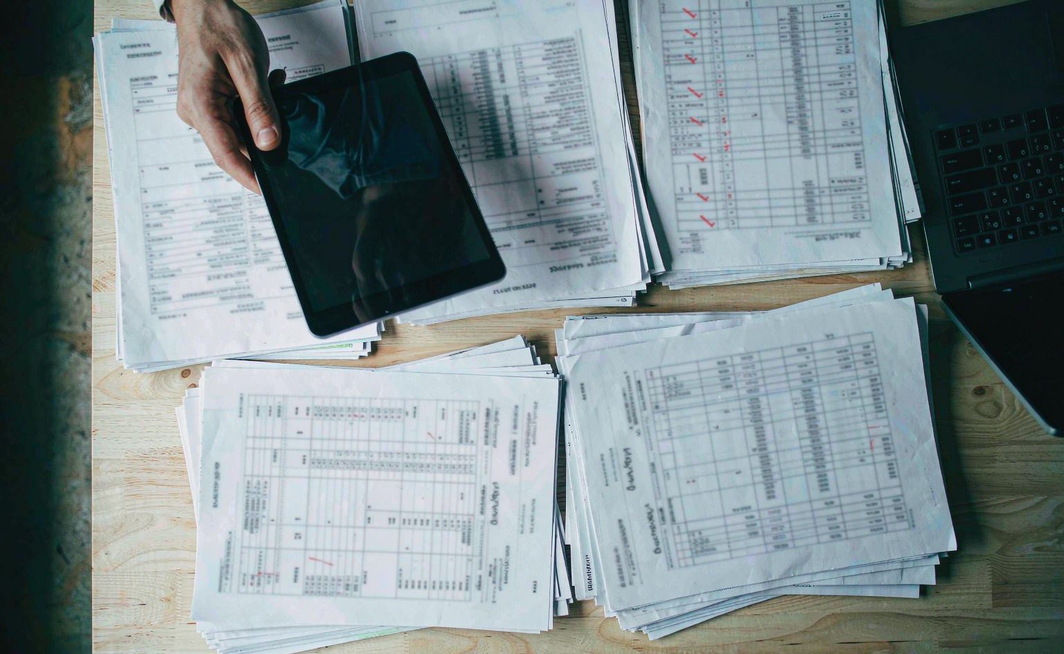 Invoice and purchase order documents laid out on a desk next to a tablet for reconciliation review