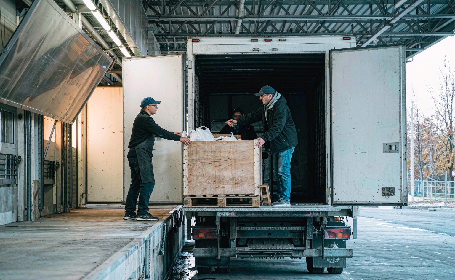 Delivery driver handing crates to a store associate at the back entrance of a retail location