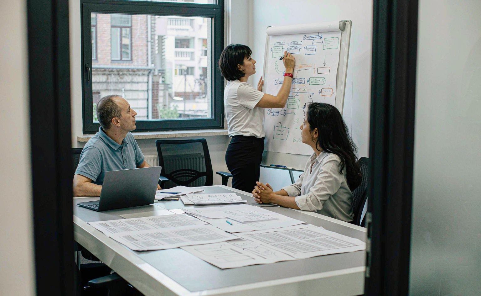 Operations team discussing a workflow plan together at a meeting table with laptops